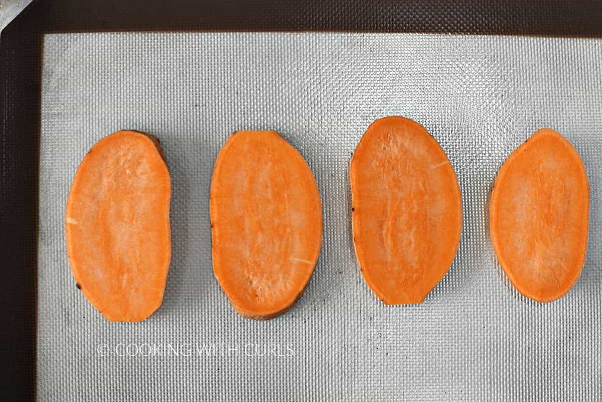Four slices of sweet potato on a silicone lined baking sheet.