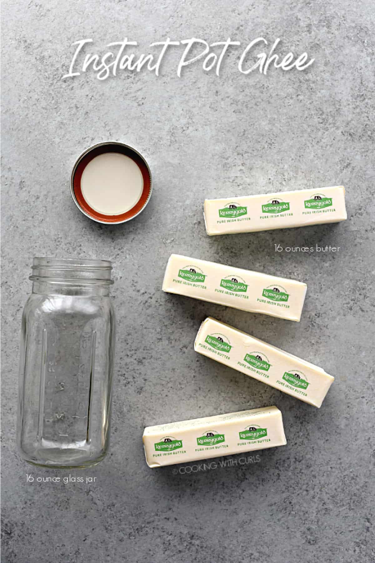 looking down on four sticks of butter and a glass jar with lid laying on a gray, stone surface.