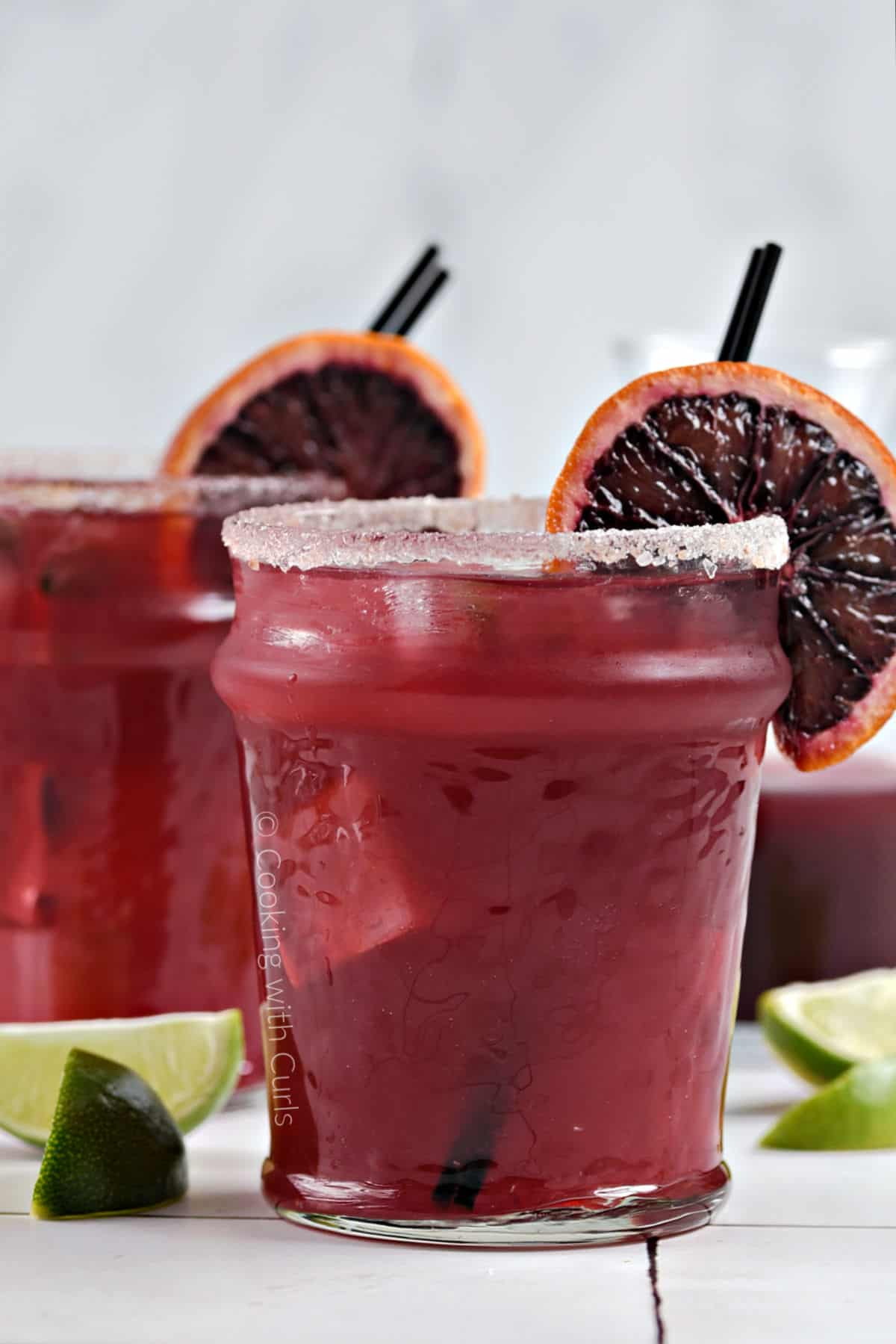 Side view ofTwo blood orange margaritas in short glasses garnished with an orange wheel and a sugar rim.