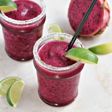 Two bright pink cocktails in sugar rimmed glasses with a lime wedge garnish.