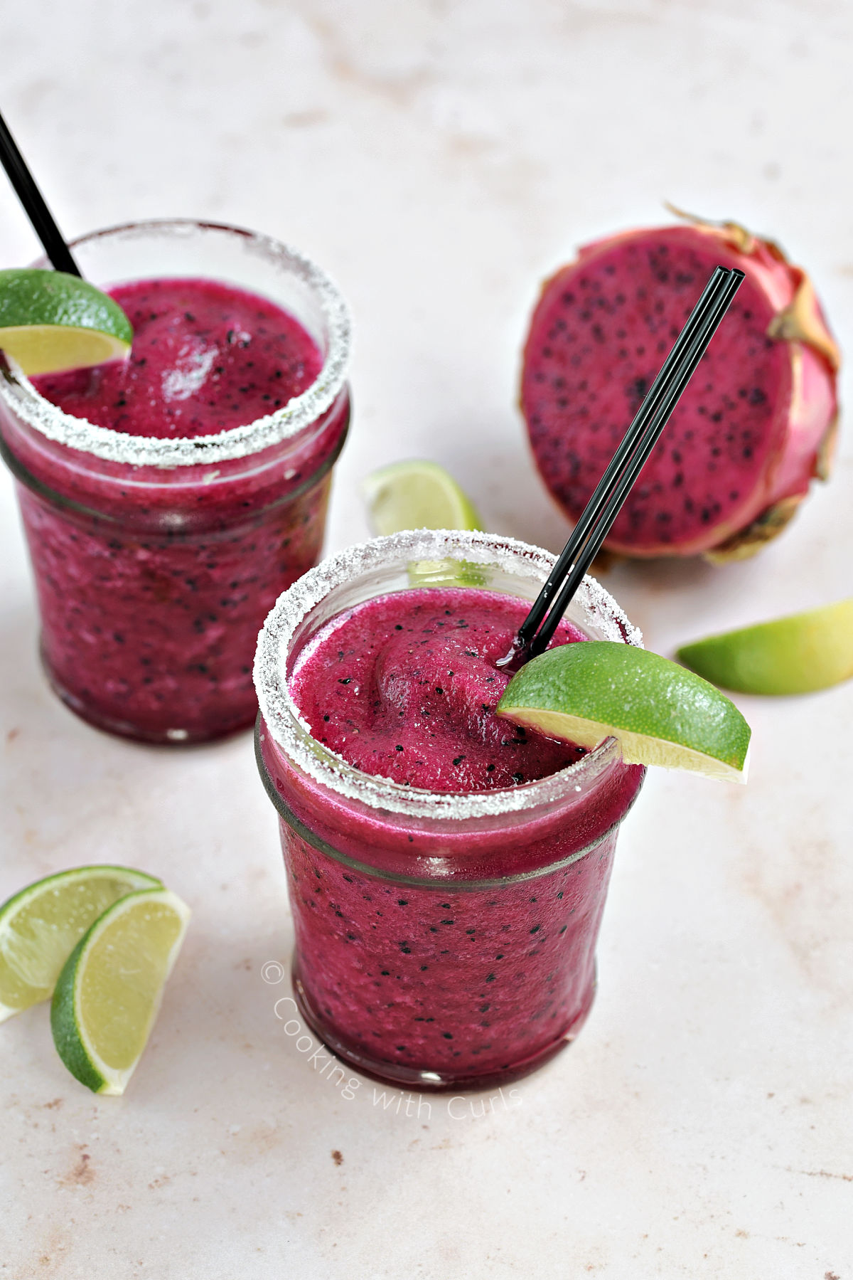 Two bright pink cocktails in sugar rimmed glasses with a lime wedge garnish.