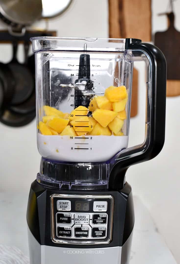 Frozen pineapple and mango chunks with coconut milk in a blender