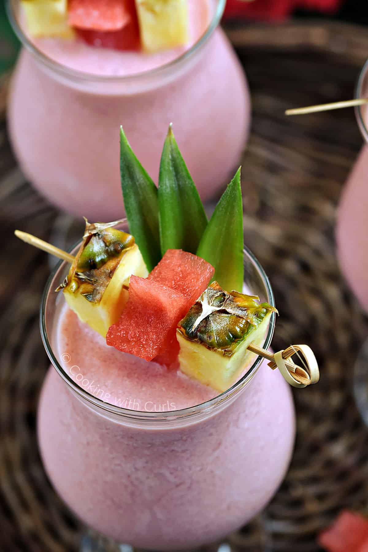 Looking down on a frozen pink drink garnished with pineapple leaves, wedges, and watermelon stars.