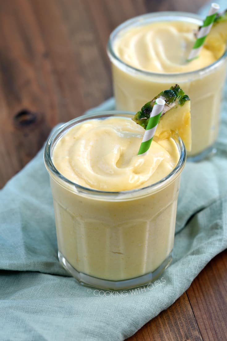 Two glasses filled with frozen Mango Pina Colada Smoothie garnished with a pineapple wedge and green and white striped straw