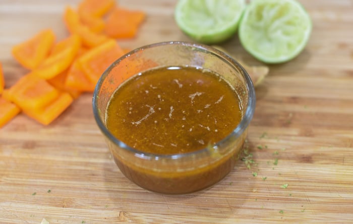 glaze in small glass bowl sitting on a wooden cutting board with orange bell pepper squares and lime halves. 