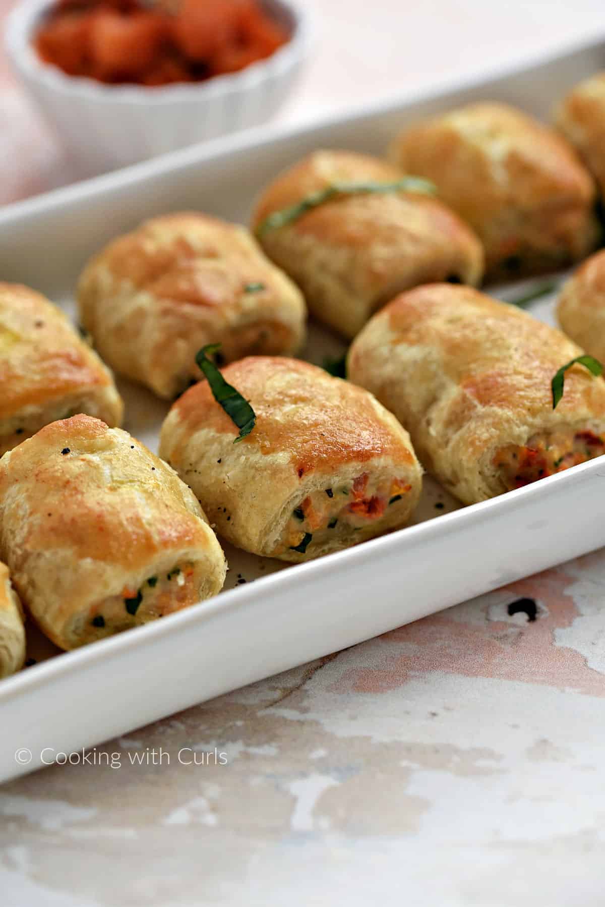 Crispy puff pastry filled with bruschetta chicken sausage rolls lined up on a serving tray.