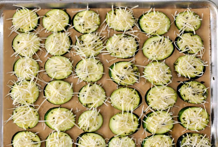Grated Parmesan cheese topped zucchini slices on a parchment lined baking sheet. 