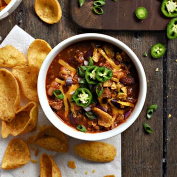 Looking down on two bowls of Guinness Beef Chili topped with cheddar cheese, green onions, and sliced jalapenos.