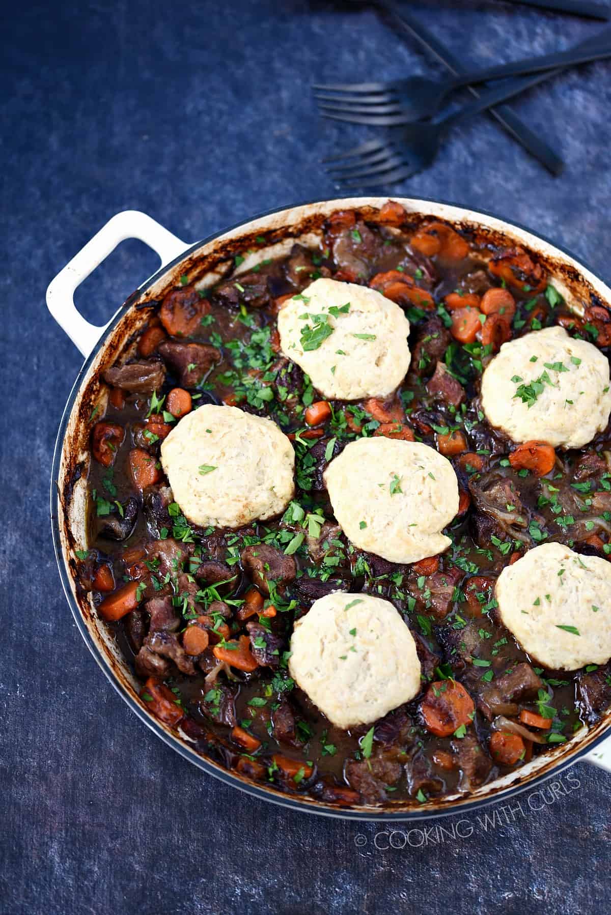 Looking down on a casserole pan filled with Guinness Beef, carrots and onions topped with Herb Dumplings.