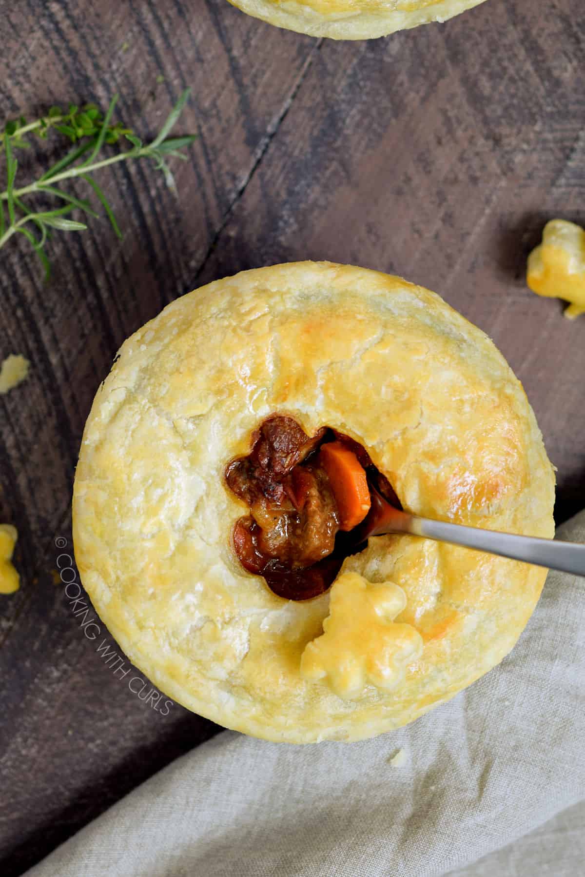 Looking down on a puff pastry topped beef stew in a blue ramekin with a spoon sticking out of the center.