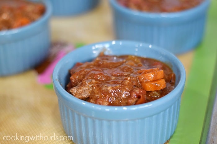 Beef stew divided between four blue ramekins on a silcone lined baking sheet.