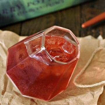 Red cocktail in a square cut glass sitting on brown paper in front of Harry Potter books.