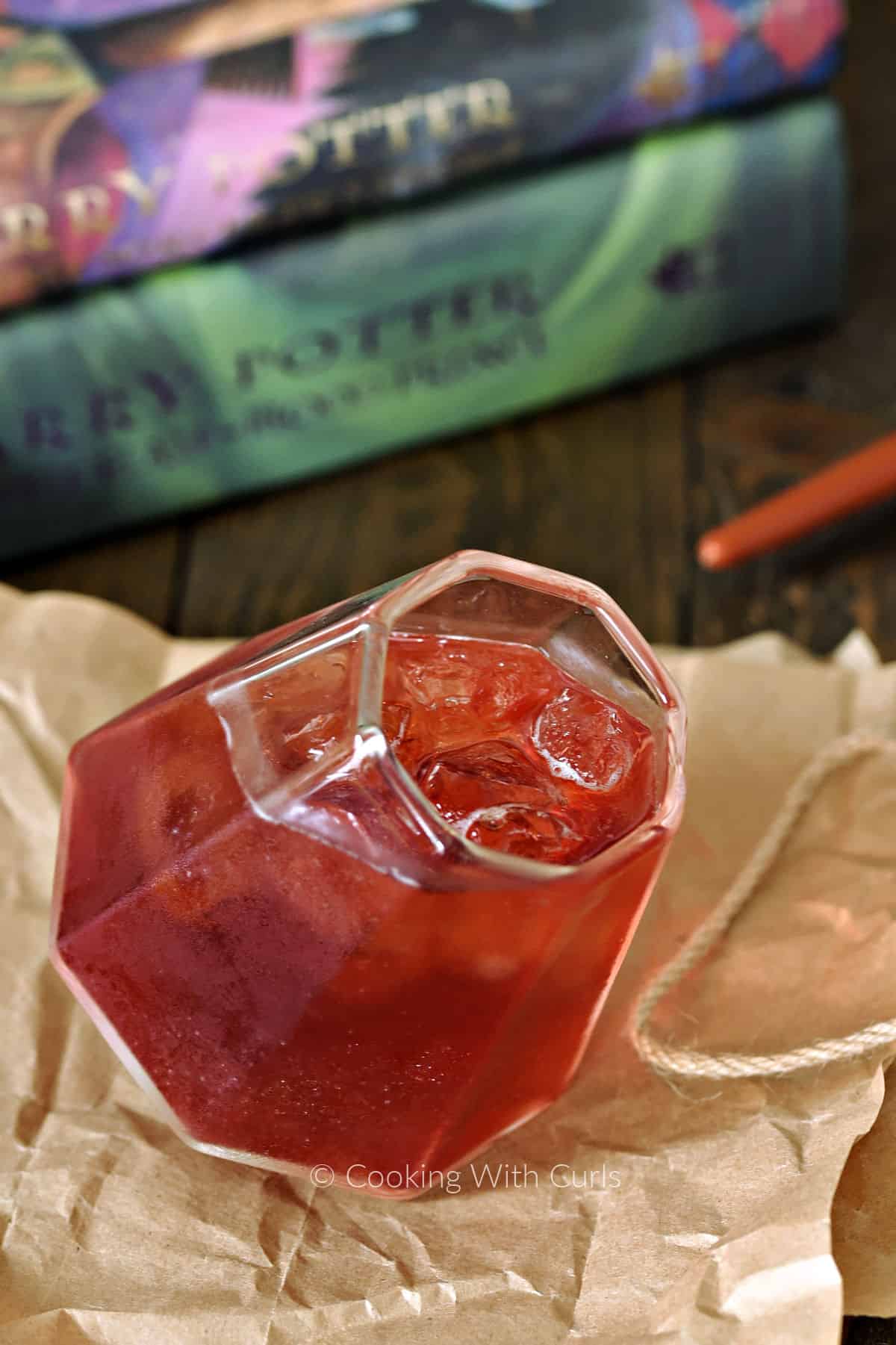 Red cocktail in a square cut glass sitting on brown paper in front of Harry Potter books.