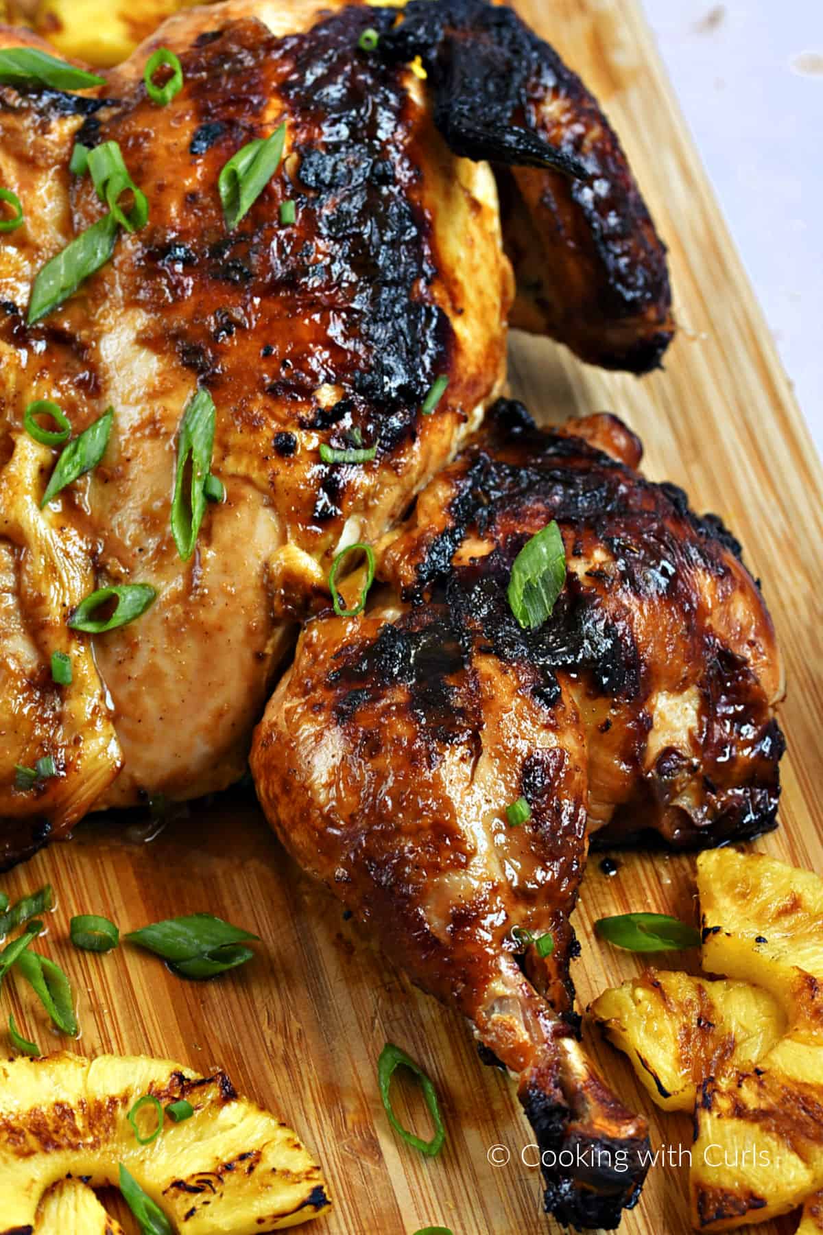 A close-up image of the right leg on a grilled whole chicken with sliced pineapple on a cutting board.