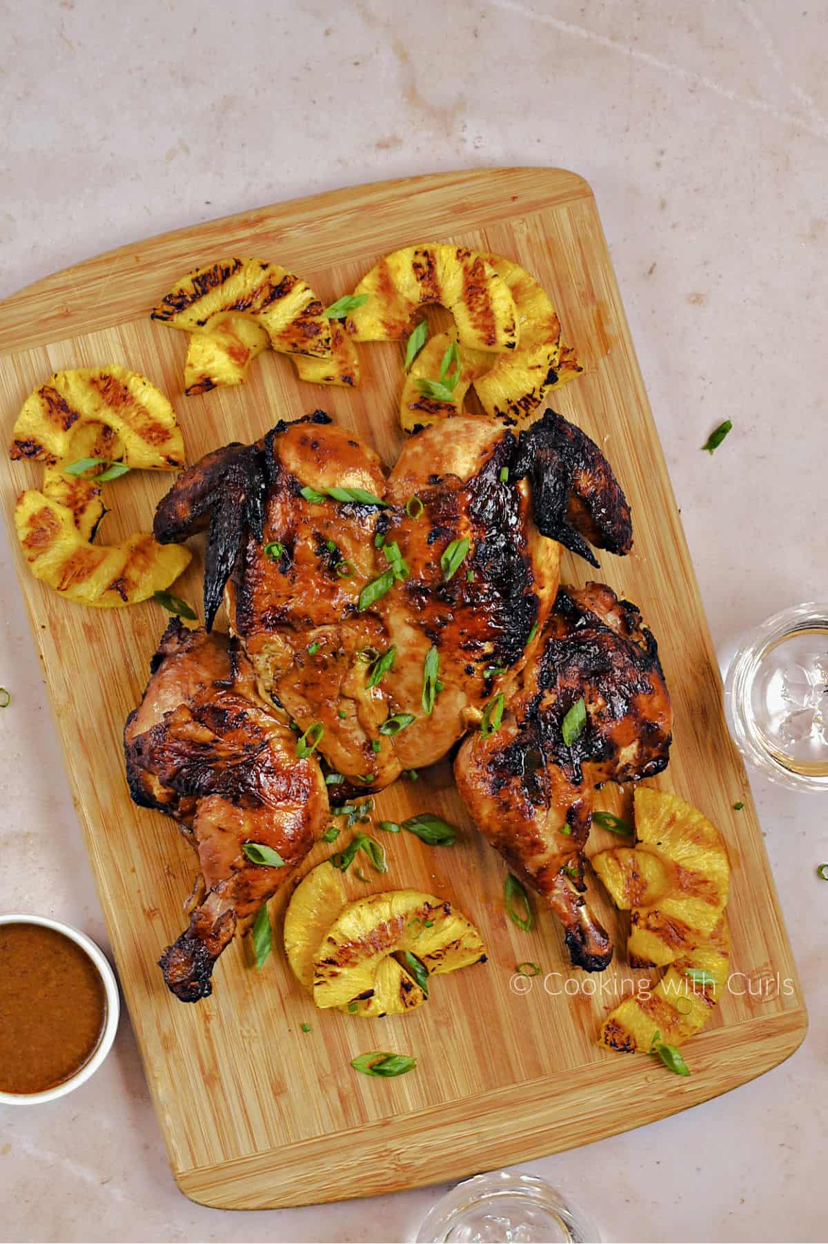 Looking down on Hawaiian Grilled Whole Chicken and Pineapple slices on a wooden cutting board. 