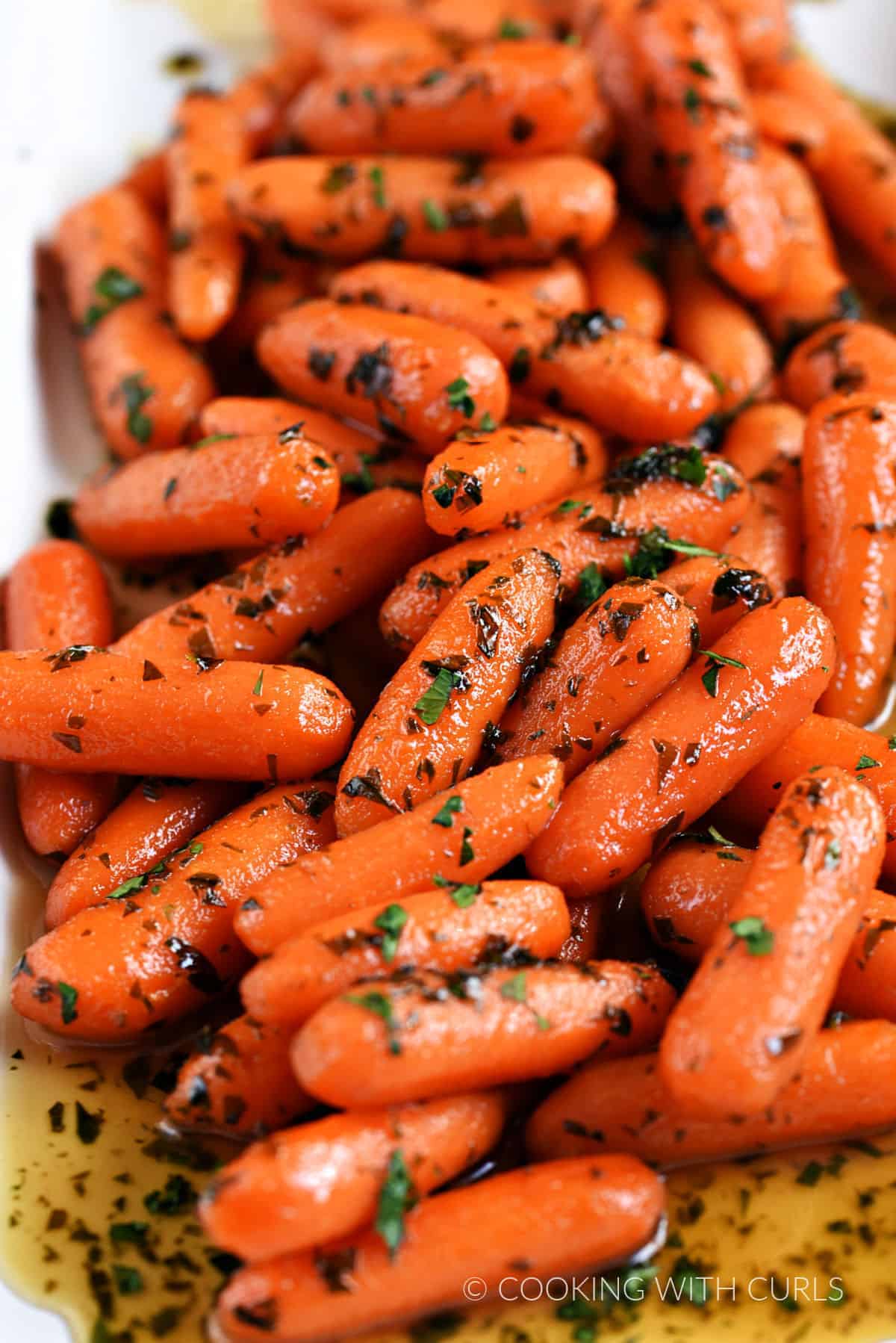 Baby carrots in a honey glaze and topped with chopped parsley on a white platter.