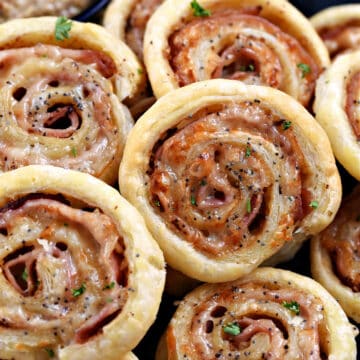 Ham and cheese pinwheels stacked on a plate with a bowl of Dijon mustard in the background.