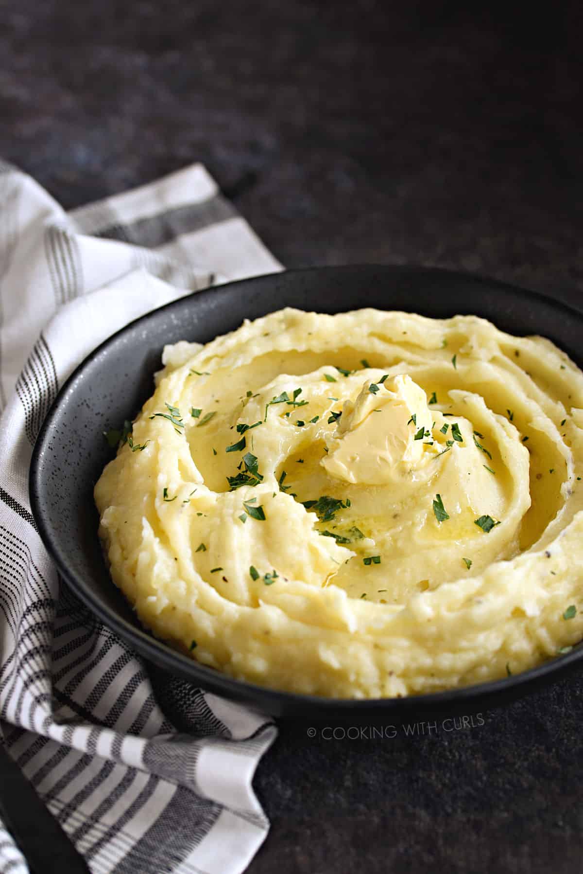 A black bowl filled with fluffy mashed potatoes topped with butter.