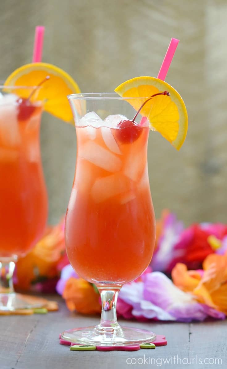 Two bright red cocktails in a hurricane glasses garnished with orange wheel and cherry.