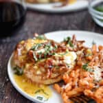 Butterflied chicken breast, goat cheese, lemon-butter sauce, sun-dried tomatoes and fresh basil on a white plate with a side of curly pasta with red sauce