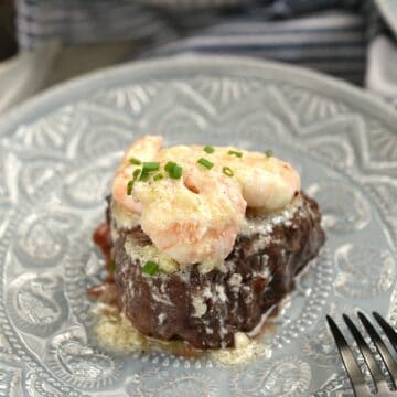 shrimp topped filet on a gray plate with a salad in a white bowl in the background