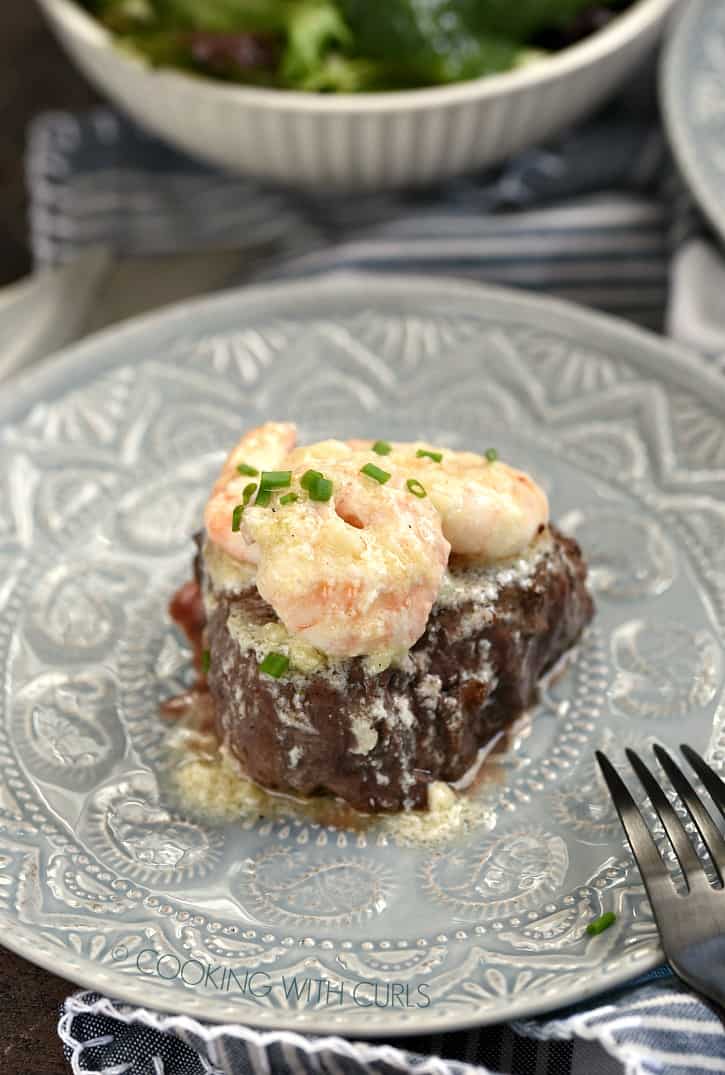 shrimp topped filet on a gray plate with a salad in a white bowl in the background