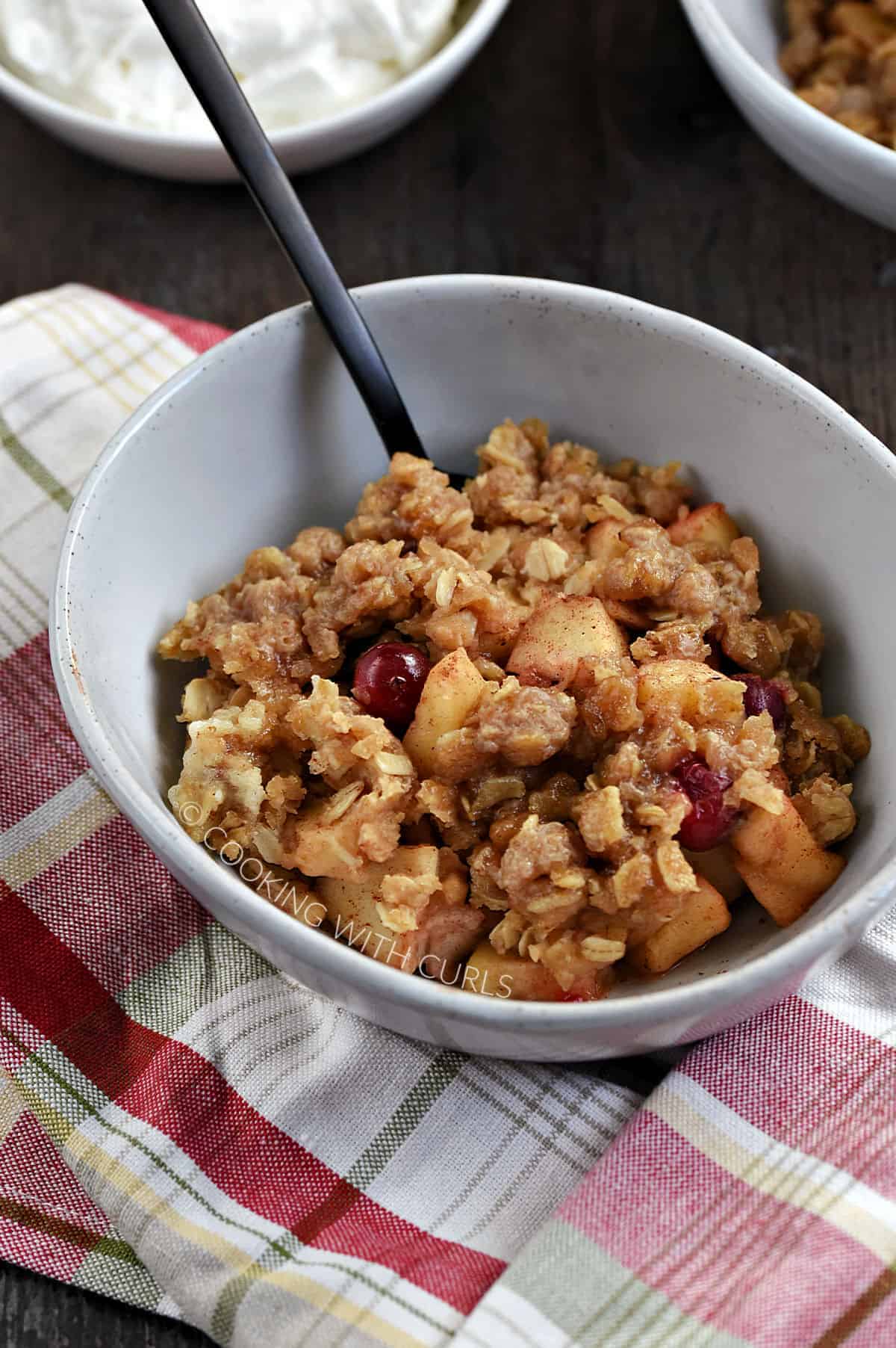 Instant Pot Apple Cranberry Crisp in a small bowl, with a bowl of whipped cream in the background.