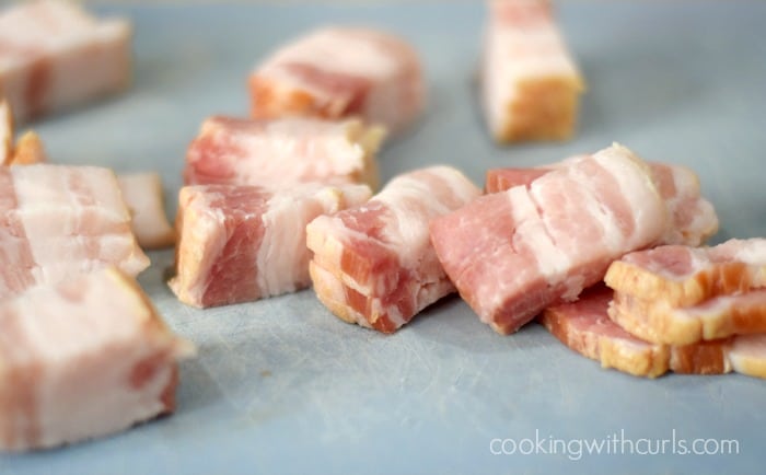 Raw bacon chunks on a cutting board.