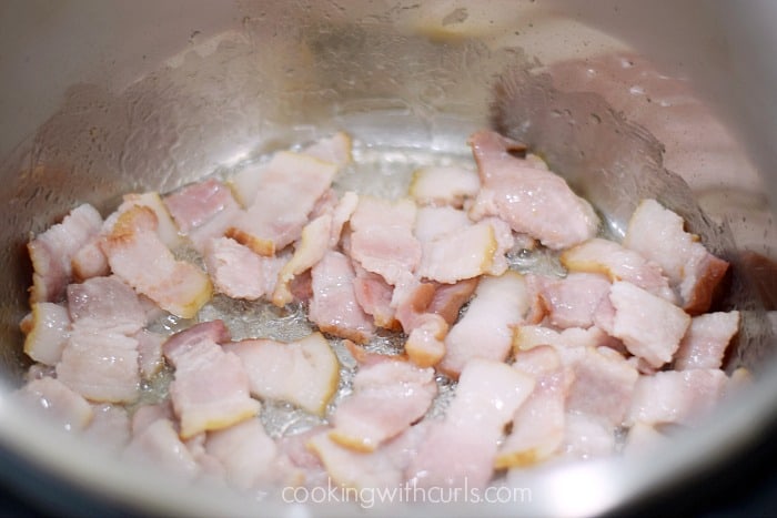 Raw bacon pieces cooking in a pressure cooker.