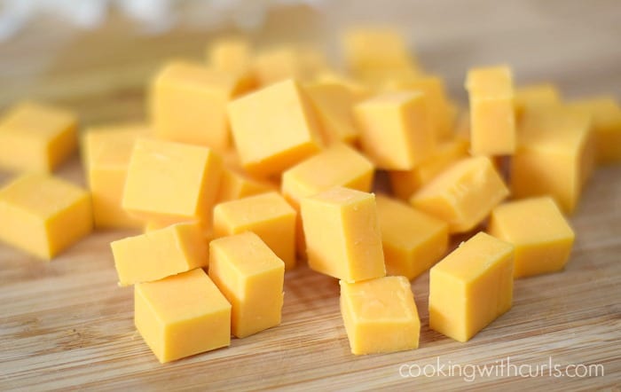 Chunks of cheddar cheese on a wooden cutting board.