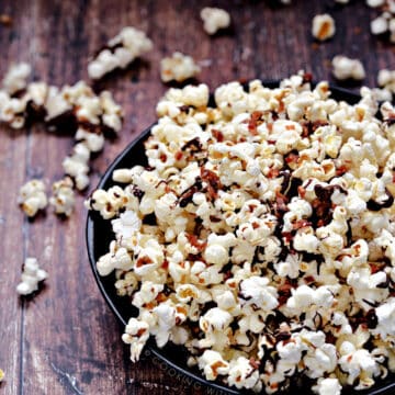 Instant Pot Chocolate Bacon Popcorn in a dark blue bowl falling out on a wooden background