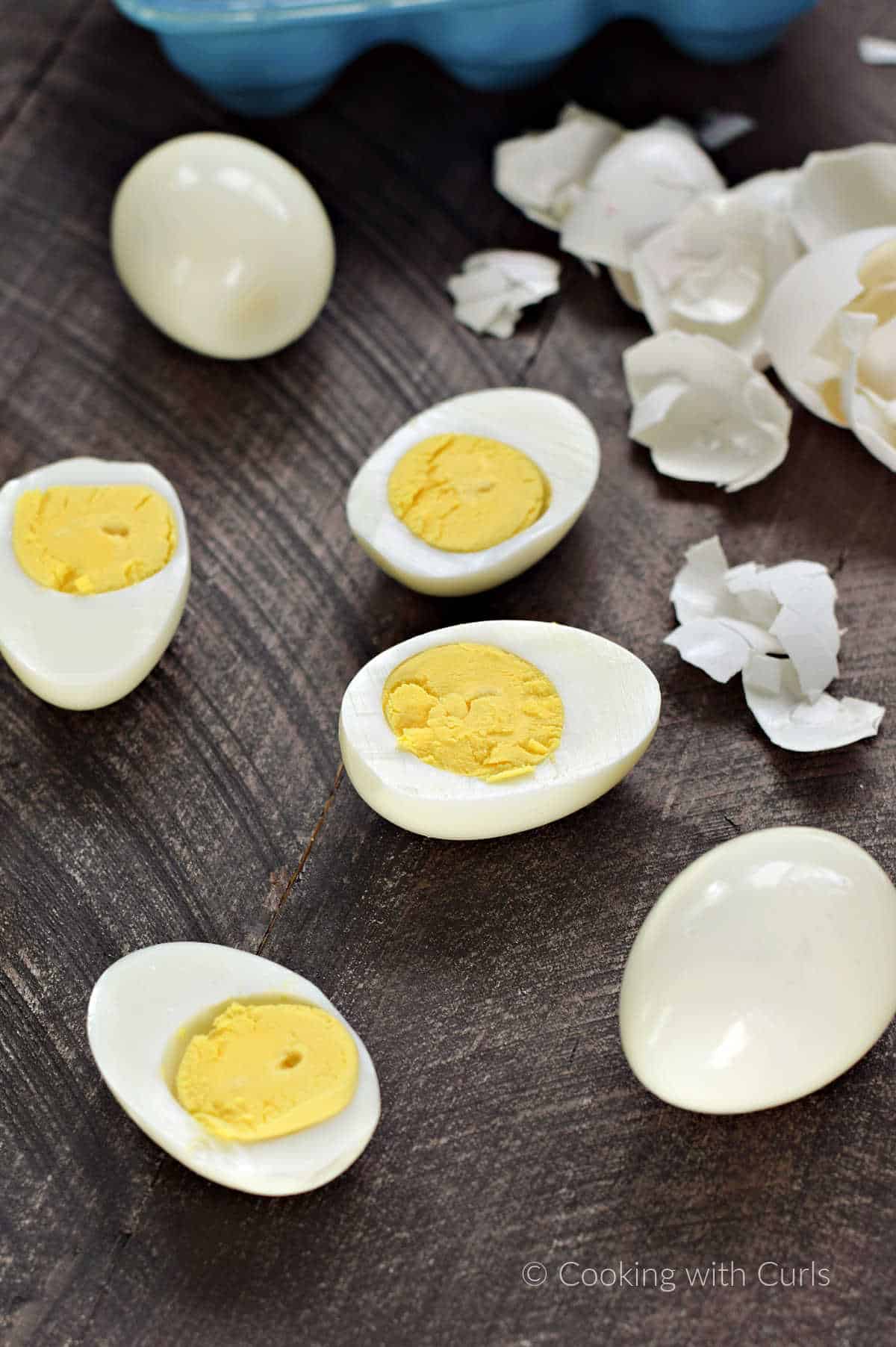 Two whole hard boiled eggs and two split in half surrounded by broken eggs shells.