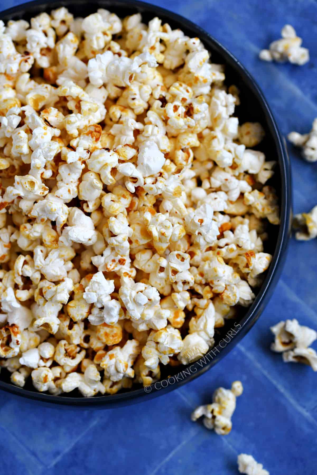 A close-up image of a bowl full of kettle corn popcorn sitting on a blue tile background.