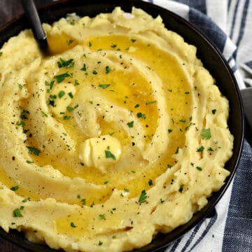 A bowl of Instant Pot Mashed Potatoes topped with melted butter and chopped parsley.