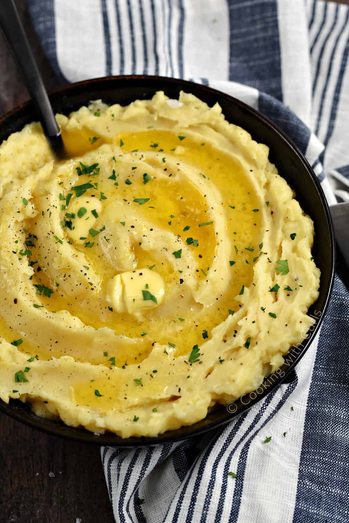 A bowl of Instant Pot Mashed Potatoes topped with melted butter and chopped parsley.