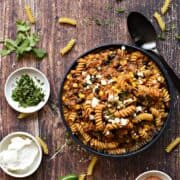 A big blue bowl filled with taco pasta topped with crumbled cheese and surrounded by bowls with taco seasoning, sour cream, and chopped cilantro with title graphic across the top.