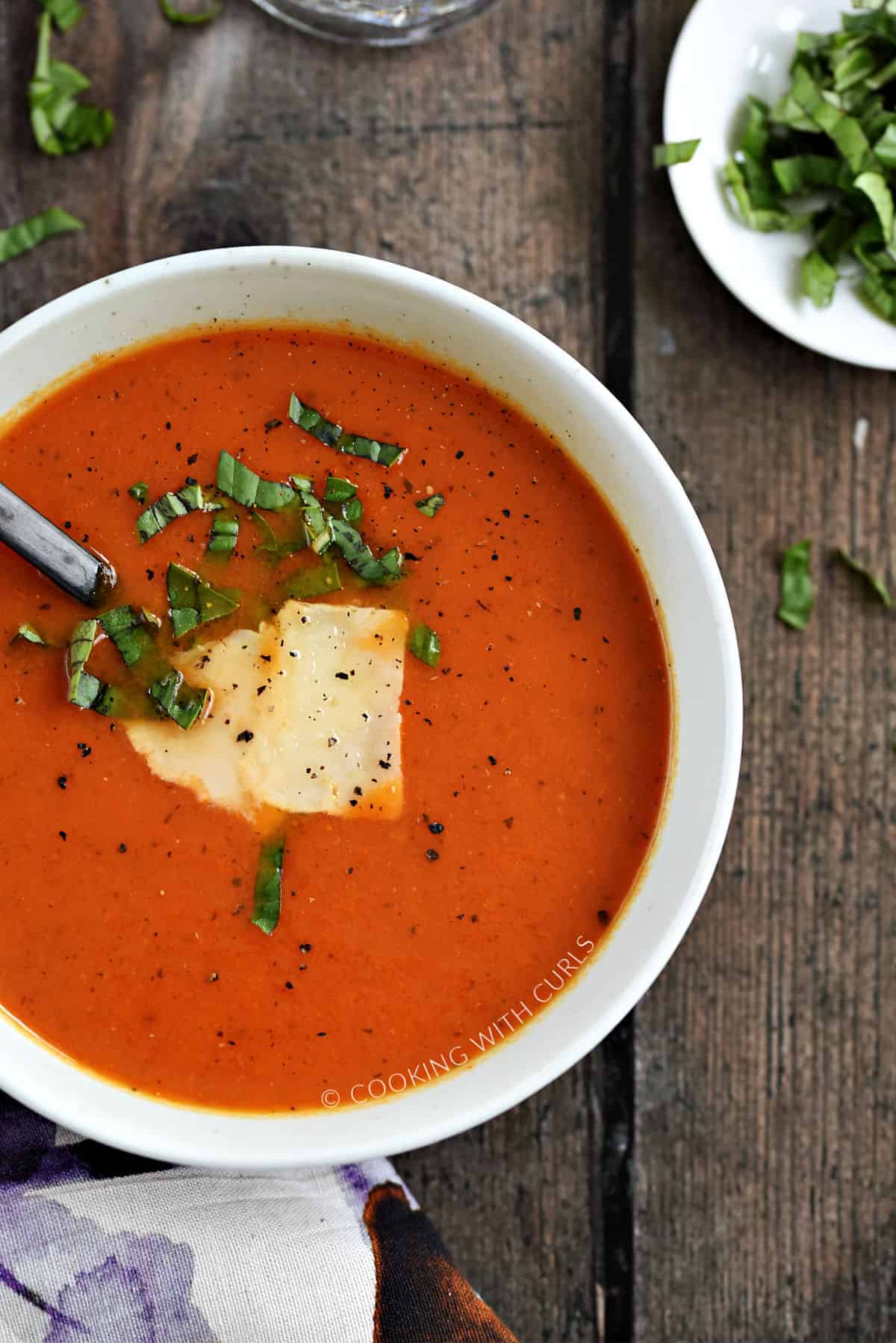 Looking down on a bowl of tomato soup topped with shaved parmesan, fresh basil, and cracked pepper.