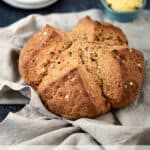 Irish Brown Soda Bread on a beige napkin with white plates and softened butter in the background.