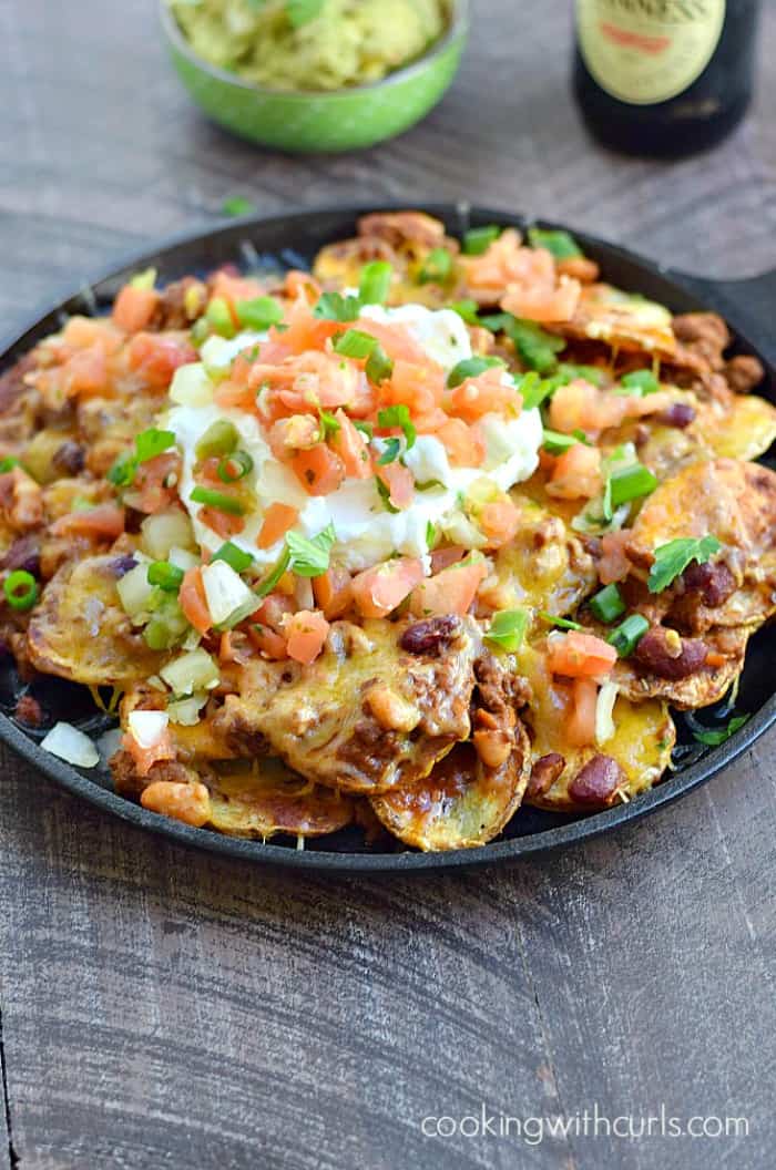 potato slices topped with chili, cheese and sour cream served in a cast iron skillet with a bottle of guinness in the background