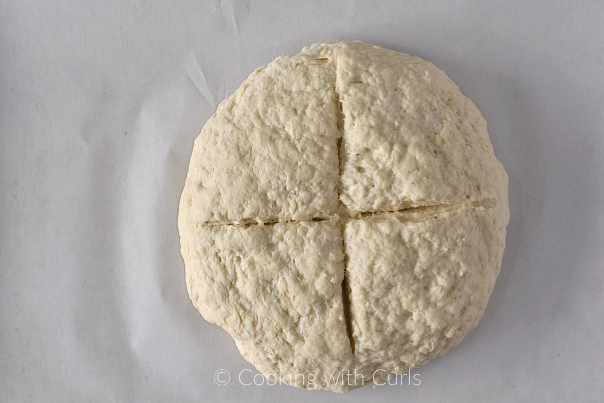 Irish soda bread dough on a parchment lined baking sheet with a deep cross cut into the top. 
