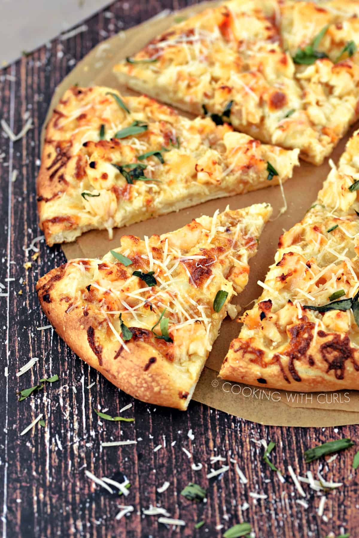 A Lobster Pizza cut into 8 slices sitting on parchment paper circles and sprinkled with tarragon and Parmesan cheese shreds.