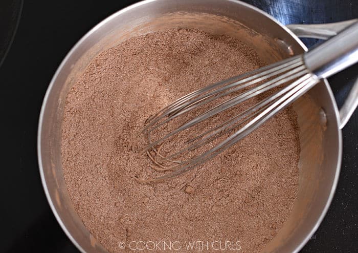 looking down on cocoa powder, flour, salt and sugar mixed together with a wire whisk in a saucepan. 