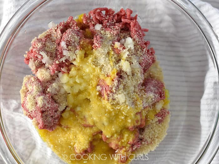 Looking down on ground beef, panko, egg and onion in a glass bowl. 