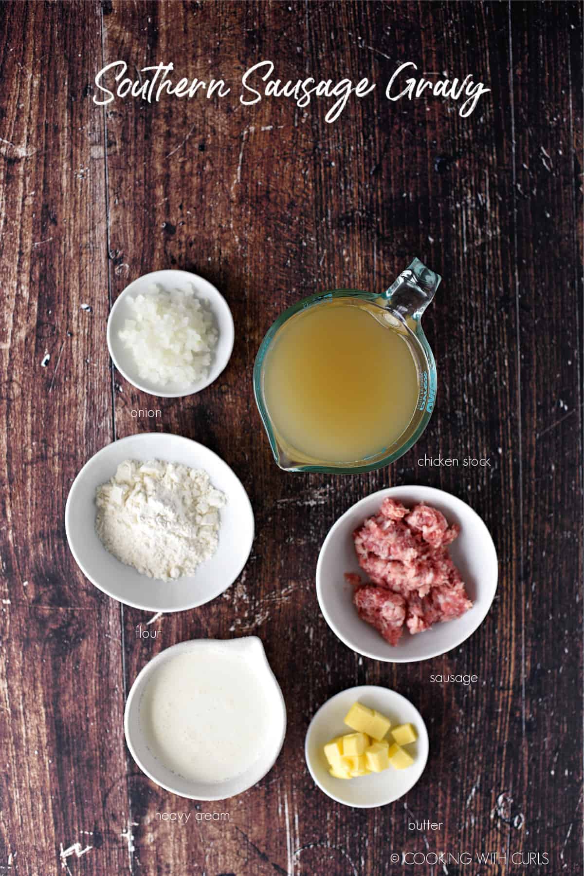 looking down on the ingredients needed to make southern sausage gravy; onion, flour, heavy cream, butter, sausage and chicken stock. 