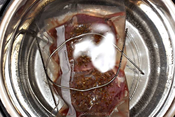 looking down on the vacuum sealed tenderloin in the instant pot with the trivet handles over the top to keep them in place. 