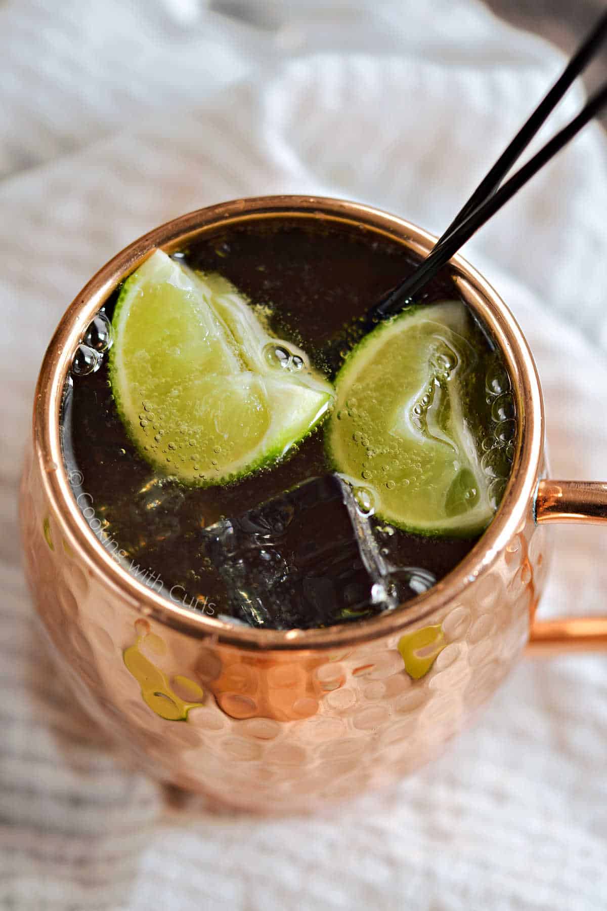 Looking into a copper mug filled with Irish Mule with ice cubes and two lime wedges. 