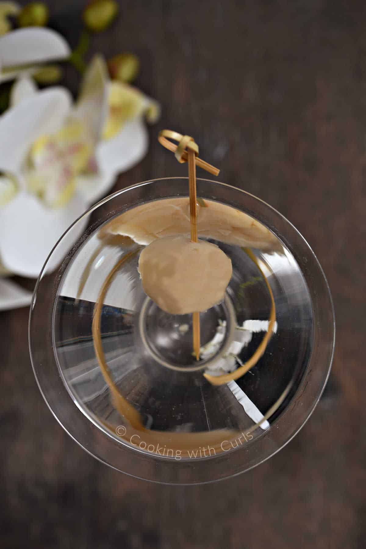 Looking down into a martini glass filled with a martini and a lychee on a bamboo pick.