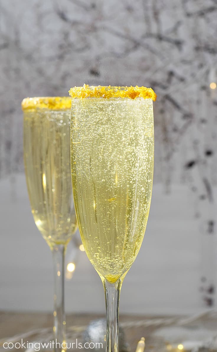 Two champagne flutes filled with gold, bubbly cocktail with gold sugar rims.