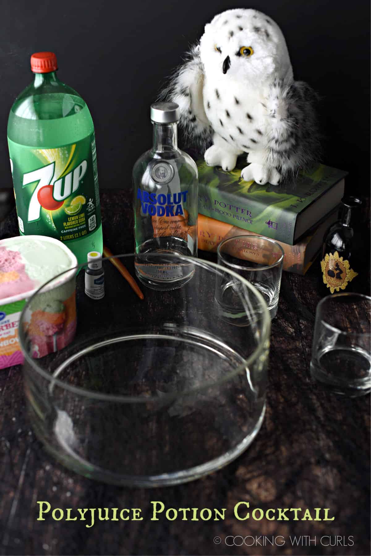 polyjuice potion ingredients; glass punch bowl, rainbow sherbet, 7up, Absolut vodka, lime green food coloring and a stack of harry potter books with a stuffed Hedwig owl on top.