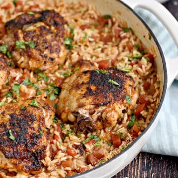 Seasoned chicken thighs on a bed of Mexican rice in a white skillet with bowls of diced avocado and crumbled cheese in the background.